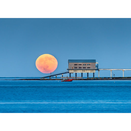 Strawberry Moonrise rising behind a coastal industrial building with the Wight bridge and boat in the foreground, captured by Available Light Photography at Bembridge Lifeboat Station.