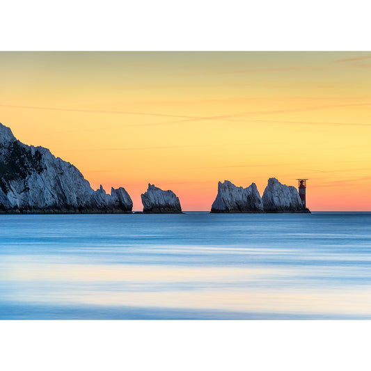 Tranquil sunset over a smooth sea with silhouetted rock formations and a small structure on The Needles' horizon captured by Available Light Photography.