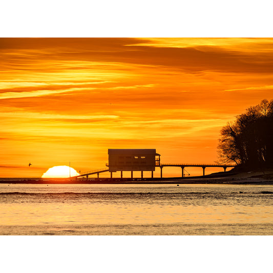 Sunrise behind a building on stilts over the water, silhouetting a pier against a vibrant orange sky. Created by Available Light Photography --> Created by Available Light Photography