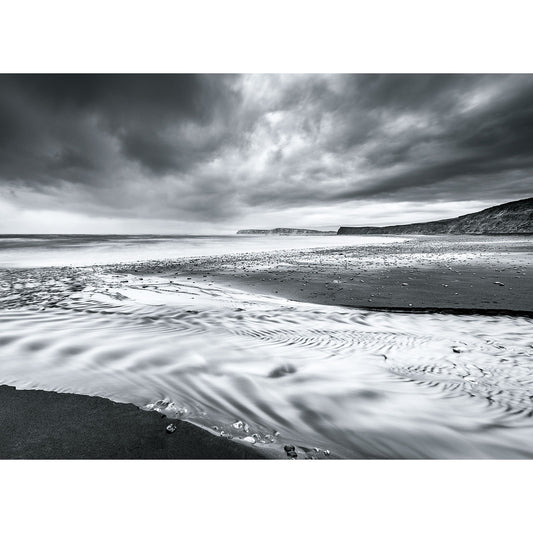 A black and white image of Compton Bay, a dramatic coastal landscape on the Isle of Wight by Available Light Photography under cloudy skies with textured sand patterns in the foreground.