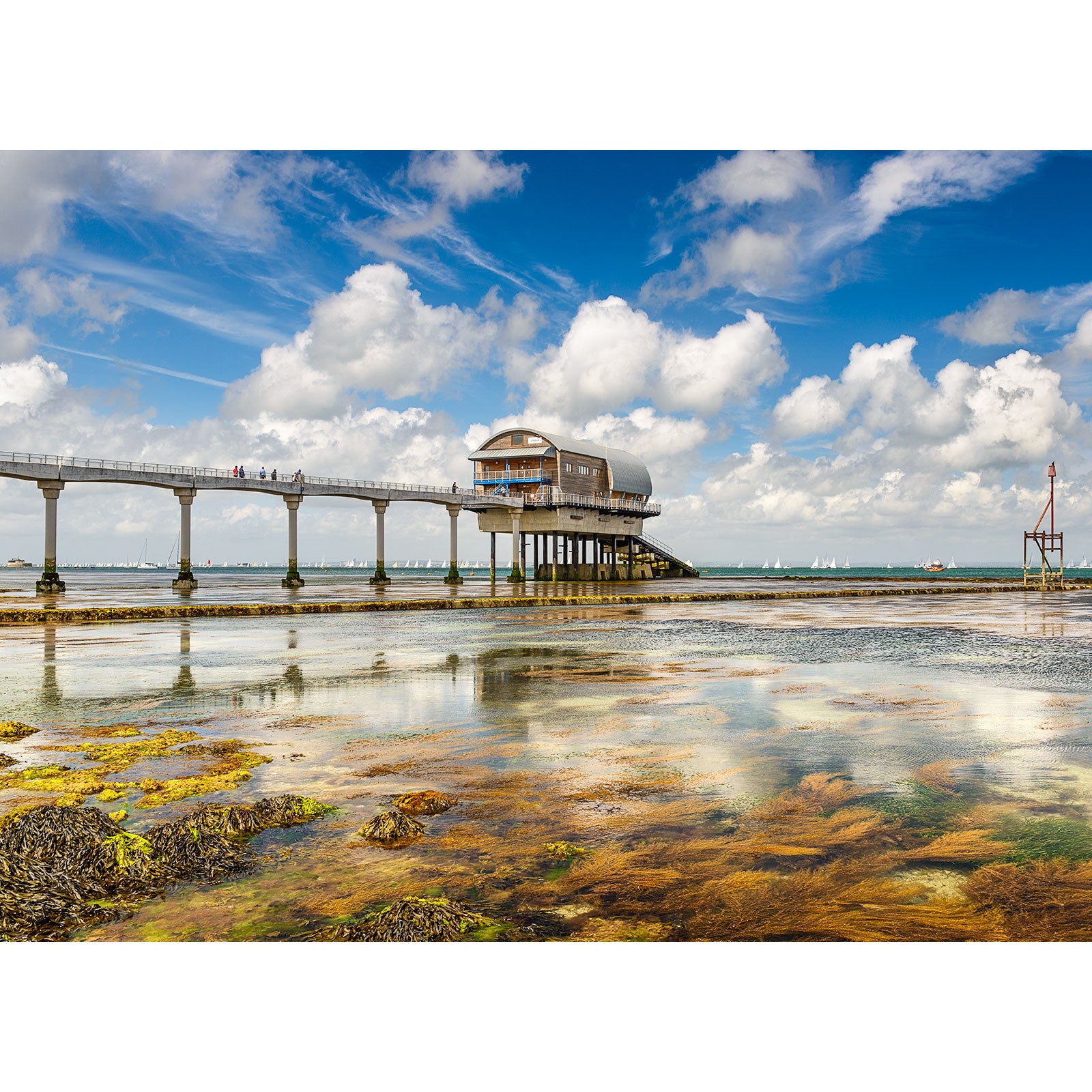 Elevated pier with a building at the end extending over shallow coastal waters off the Isle of Wight under a partly cloudy sky captured by Available Light Photography during the Round the Island Race at Bembridge Lifeboat Station.
