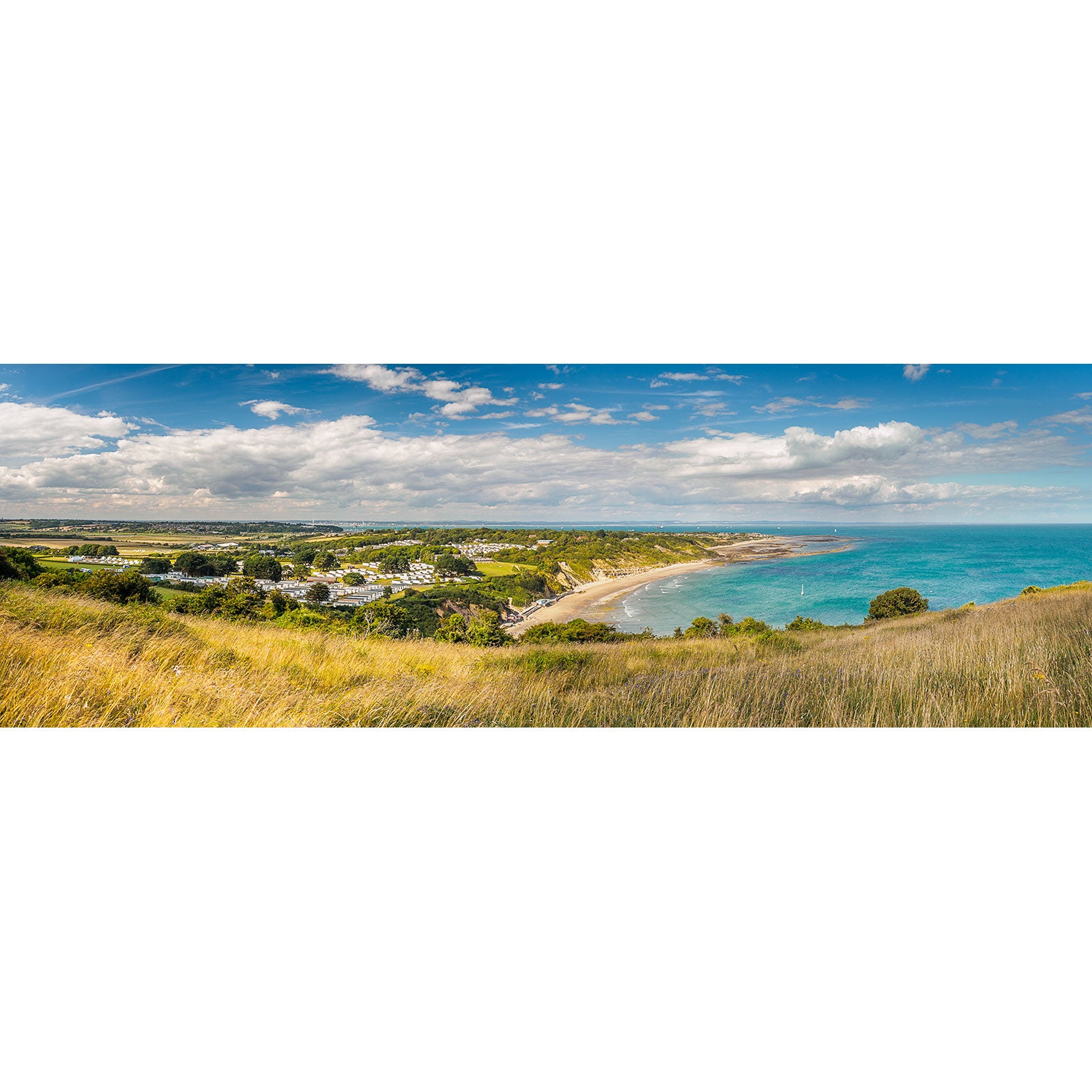 Panoramic view of Whitecliff Bay, a coastal village with a beachfront on the Isle of Wight, seen from a grassy hilltop under a partly cloudy sky, captured by Available Light Photography.