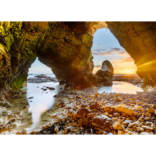 Sunset viewed through a natural archway on a rocky beach on the Isle of Wight, captured beautifully in "In the Caves, Freshwater Bay" by Available Light Photography.
