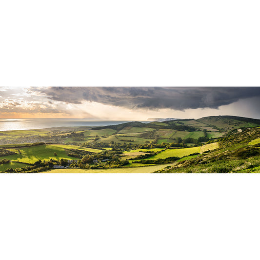 Panoramic view of a lush valley stretching towards the sea with rays of sunlight piercing through clouds on the Isle of Wight. 
Product Name: Incoming Storm, Brighstone
Brand Name: Available Light Photography