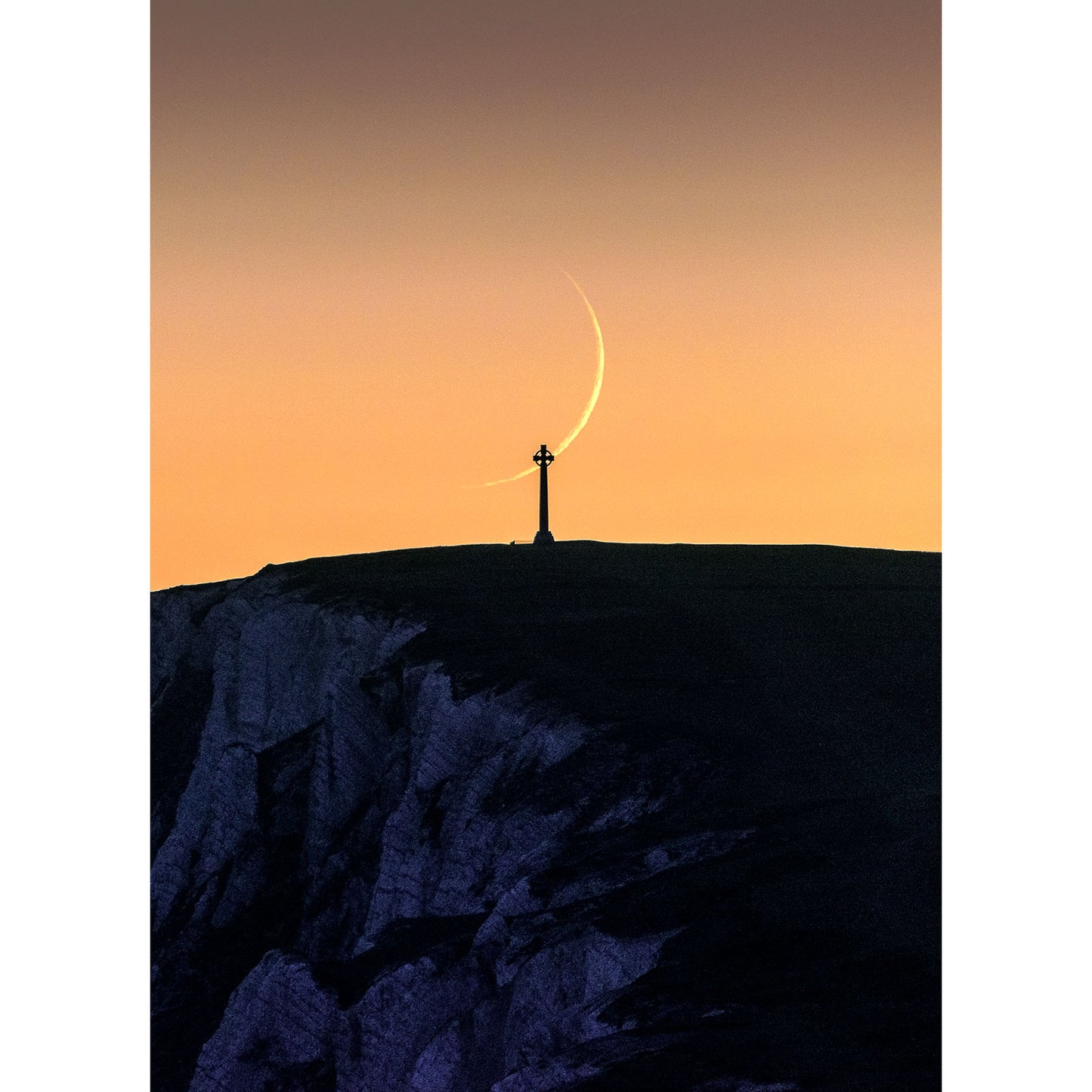 A person stands on a hilltop against a twilight sky with a Crescent Moon above, overlooking Tennyson Down on the Isle of Wight captured by Available Light Photography.