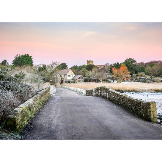 A serene winter sunrise over a rural road leading towards a village with a church steeple in the distance on the Isle of Wight by Available Light Photography's The Causeway, Afton.