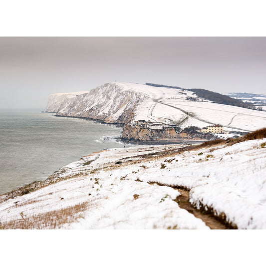 A snowy coastal landscape with cliffs and a building near the shoreline on the Tennyson Down by Available Light Photography.