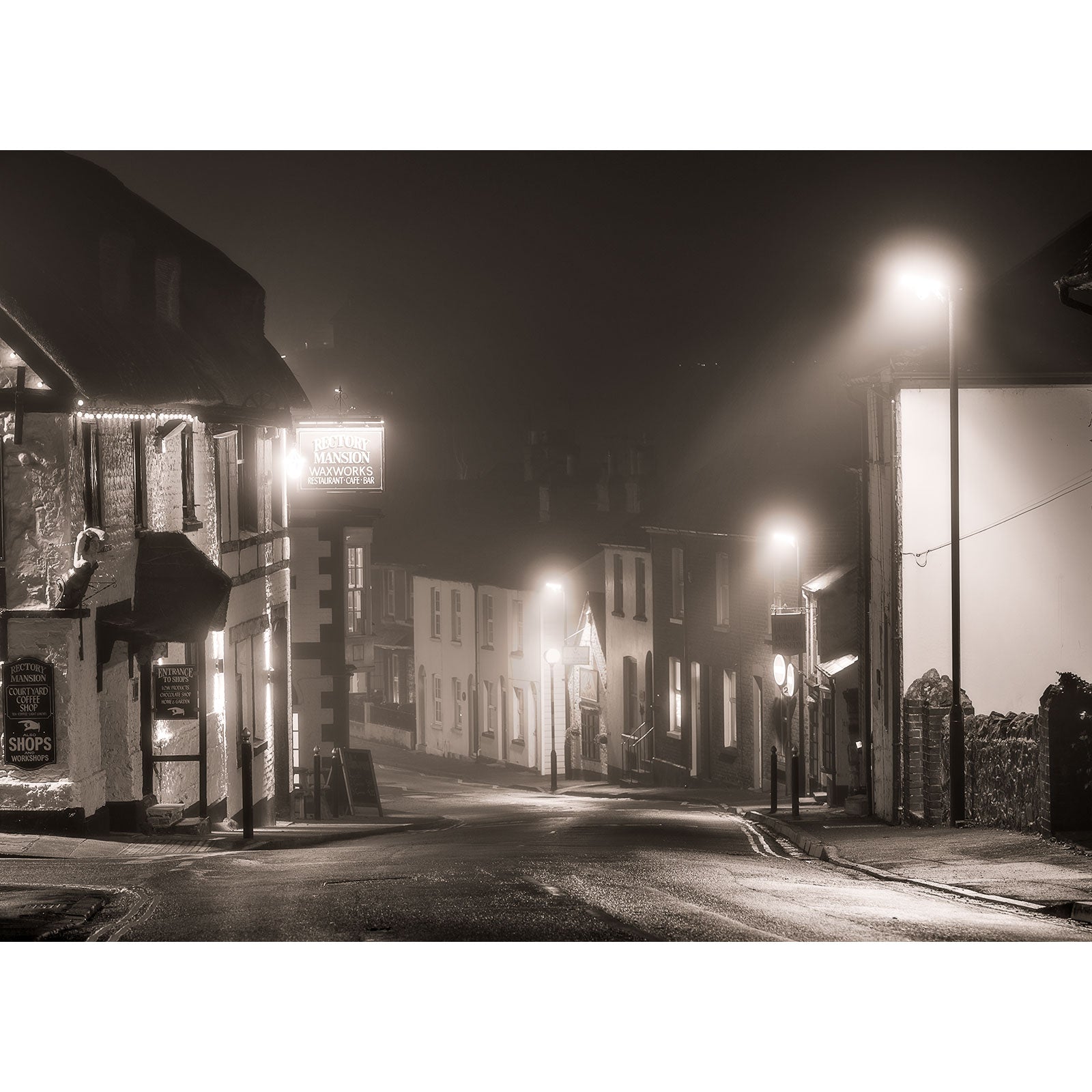 A Brading misty street at night illuminated by streetlights with buildings on one side.