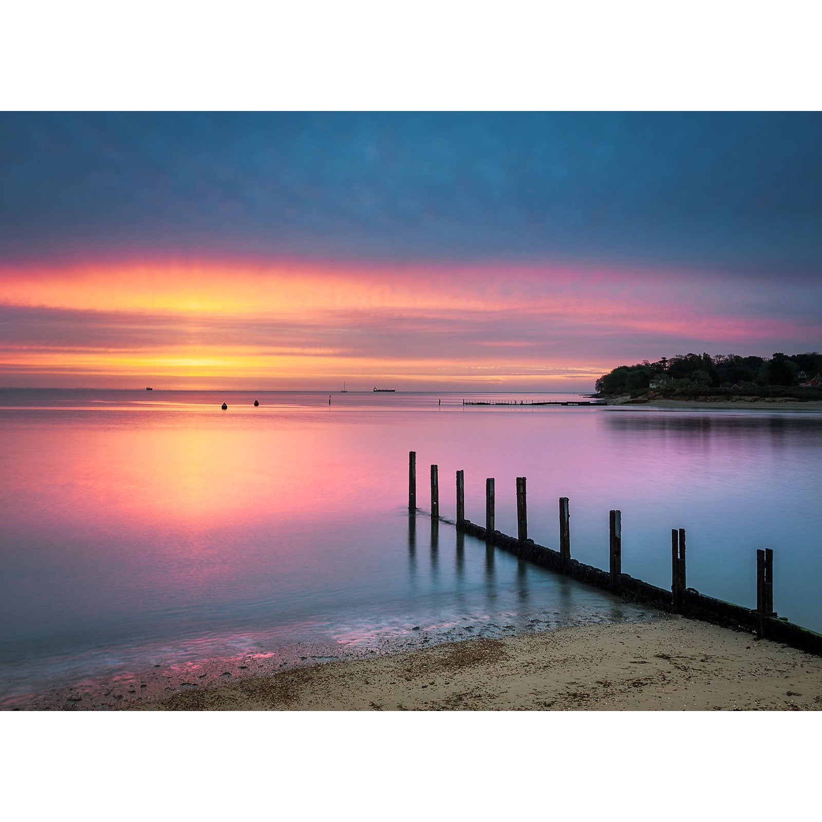 Sunset over a calm St. Helens Beach on Gascoigne Isle with a row of wooden posts leading into the water, captured by Available Light Photography.