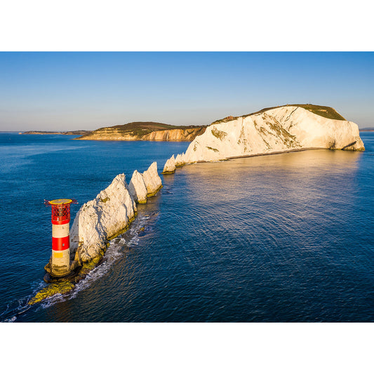 Aerial view of The Needles lighthouse on a small rocky outcrop with a backdrop of white chalk cliffs by the sea at sunset on the Isle of Wight by Available Light Photography.
