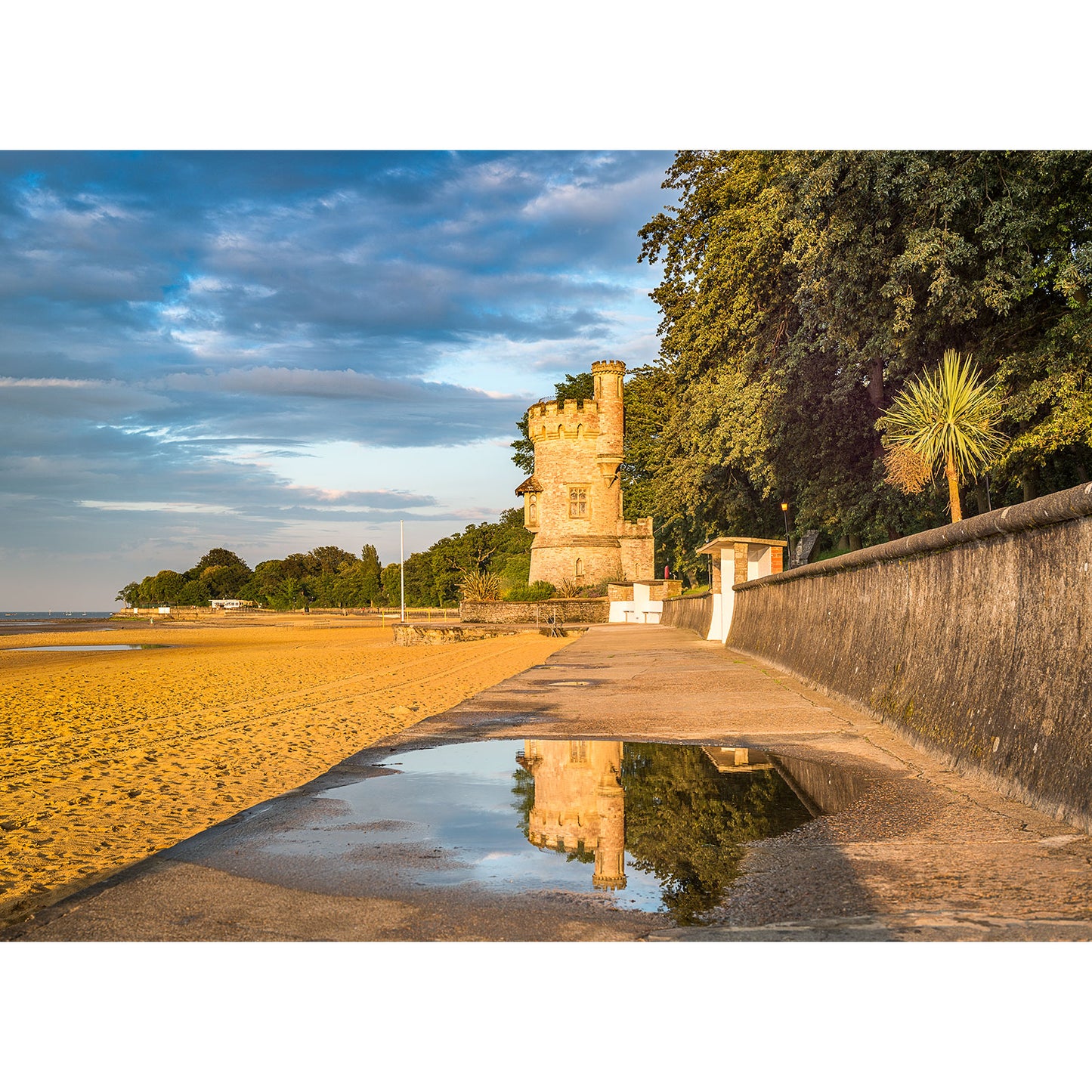 A historic Appley Tower overlooking a sandy beach with a seawall at the Isle of Gascoigne at sunset by Available Light Photography.
