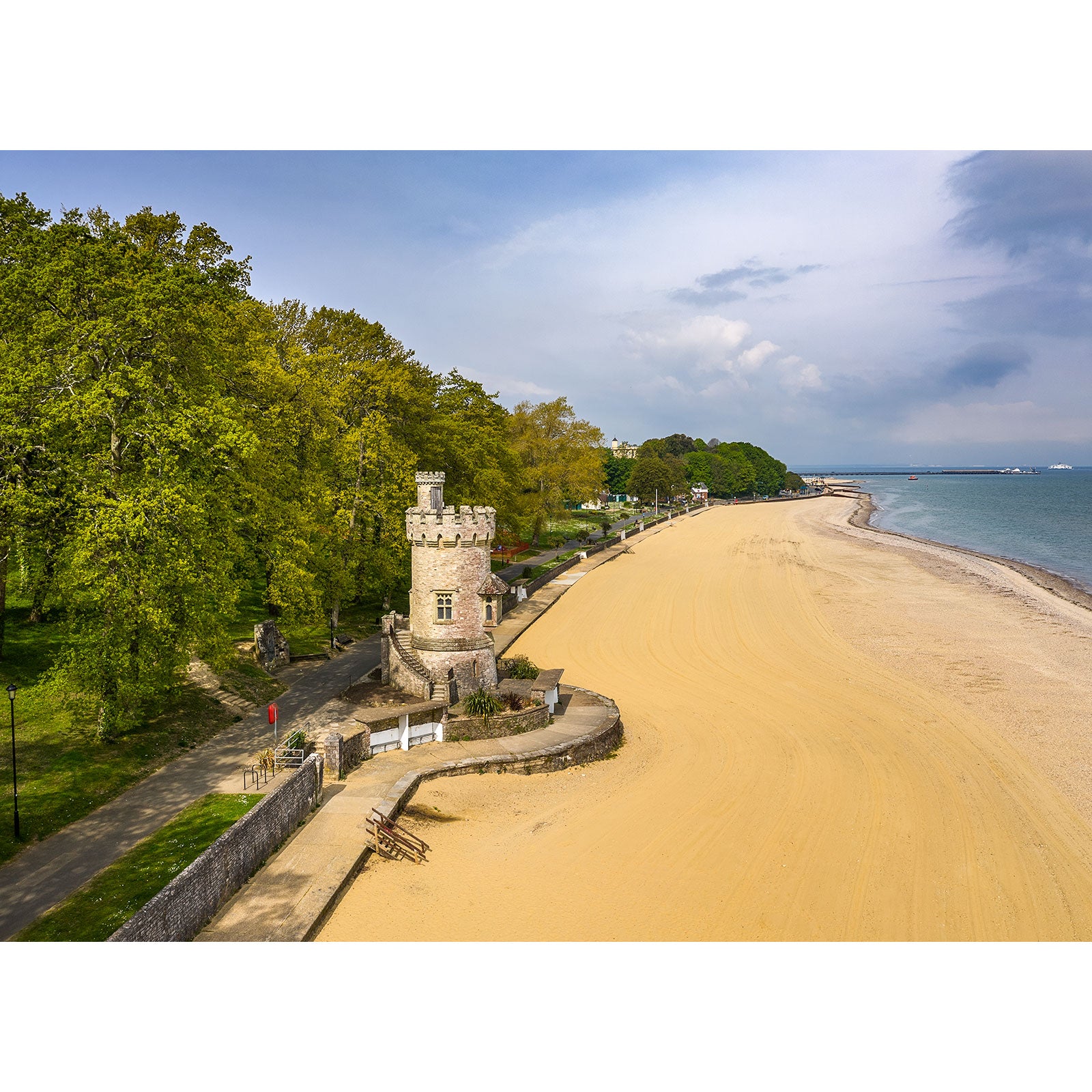 A serene beachside vista featuring the sandy shore, the Appley Tower, and a tree-lined promenade under a partly cloudy sky captured by Available Light Photography.