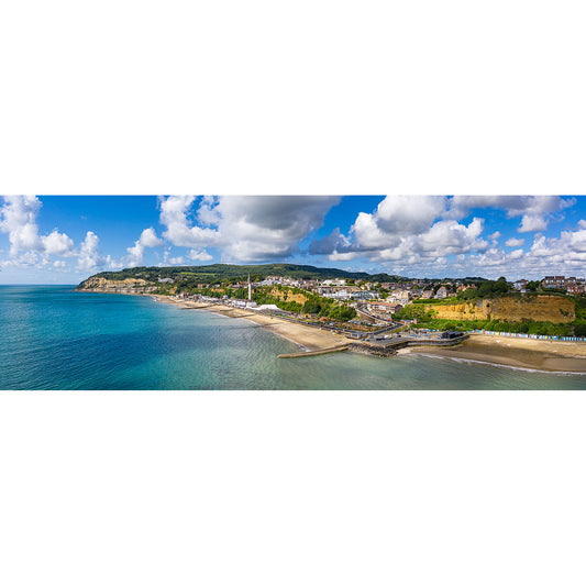 Scenic aerial view of Shanklin with a beachfront, promenade, and surrounding cliffs under a partly cloudy sky by Available Light Photography.