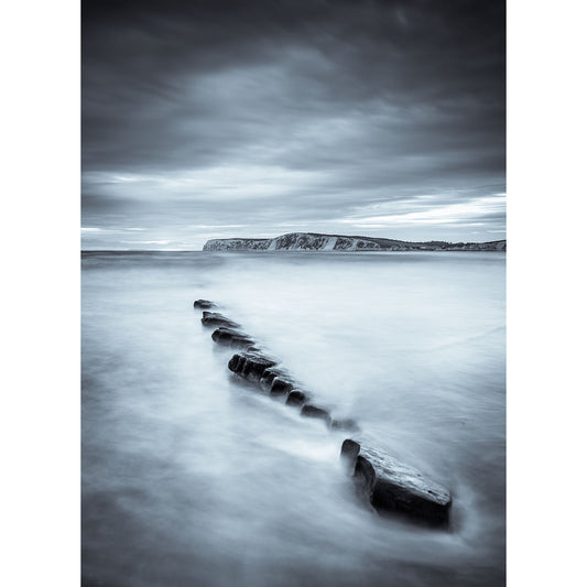 Long exposure of a serene seascape at Compton Bay with wooden groynes leading towards a distant cliff on the Isle of Wight under a cloudy sky by Available Light Photography.
