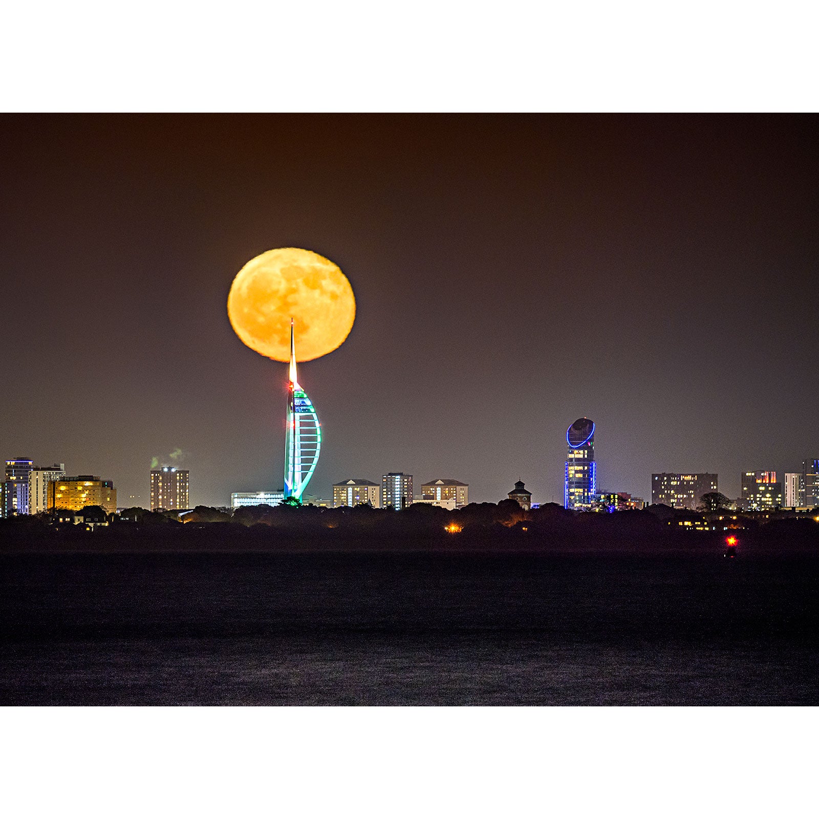 A Moonrise rising behind a city skyline with an illuminated tower on Gascoigne Isle, captured by Available Light Photography.