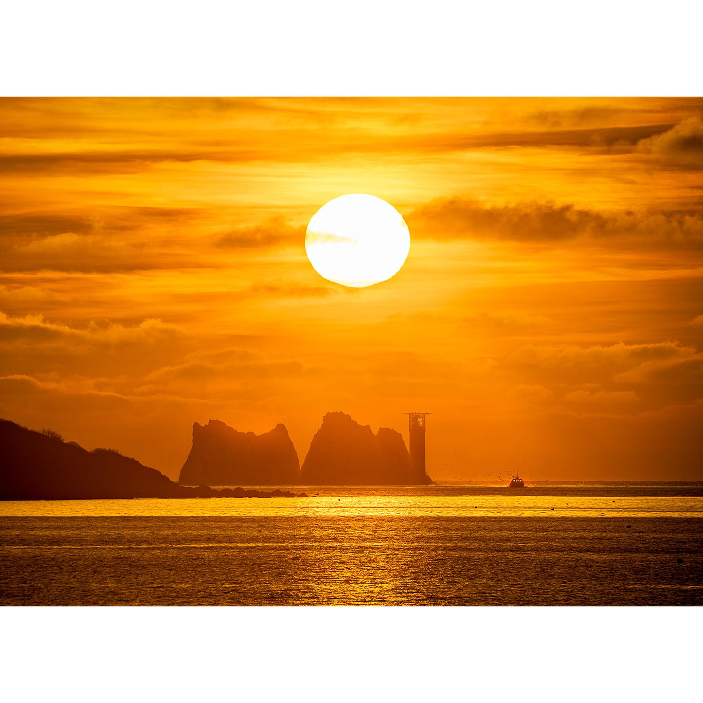 A Sunset over The Needles with silhouettes of cliffs, a lighthouse on the Isle of Wight, and a boat in the foreground by Available Light Photography.
