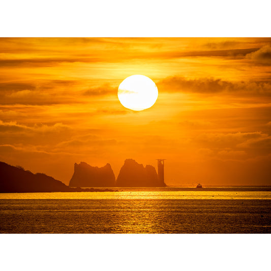 A Sunset over The Needles with silhouettes of cliffs, a lighthouse on the Isle of Wight, and a boat in the foreground by Available Light Photography.