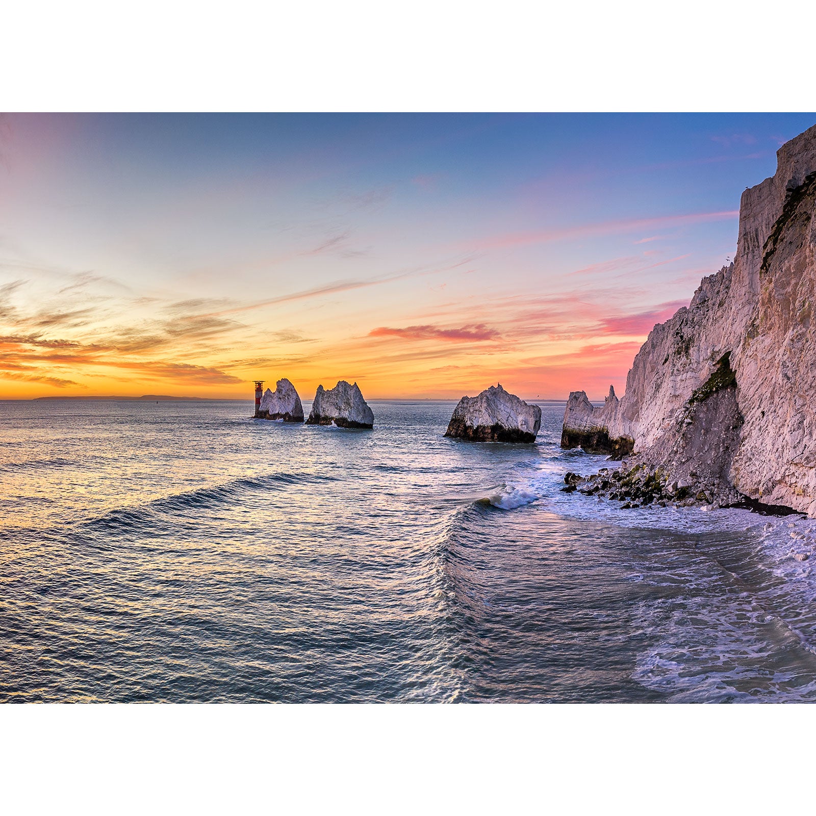 A tranquil sunset over a coastal seascape with waves breaking near the shore and rock formations in the Isle of Wight captured by Available Light Photography's The Needles.