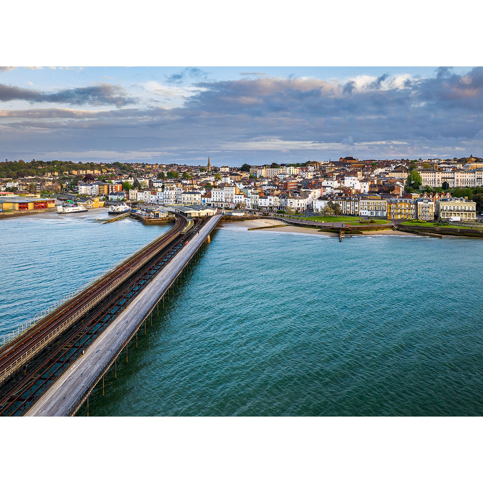 Aerial view of a coastal town with a long pier extending into the sea at dusk, captured by Steve using Ryde from Available Light Photography.
