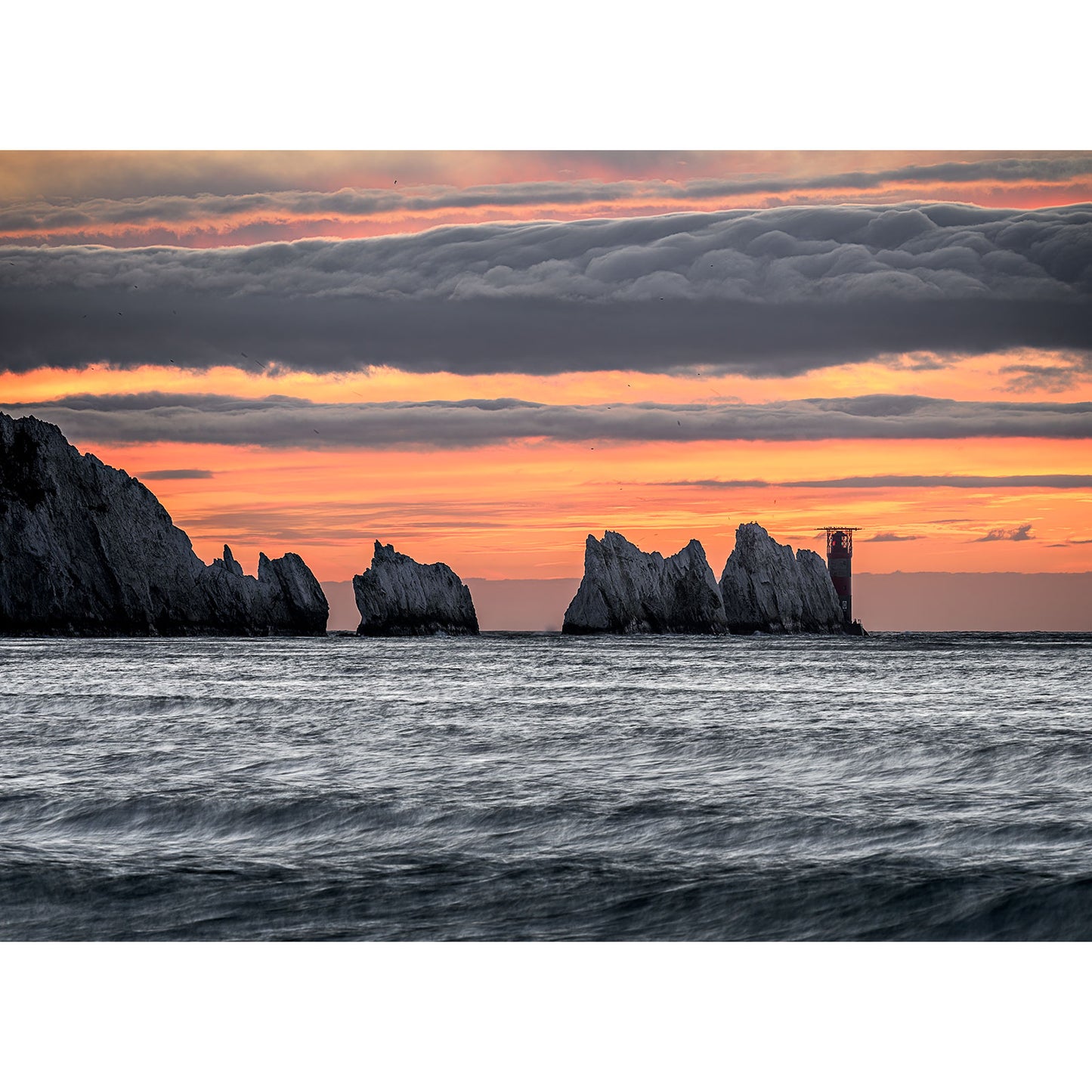 Dramatic sunset over rugged cliffs by the sea with layered clouds in the sky at Gascoigne captured by The Needles from Available Light Photography.