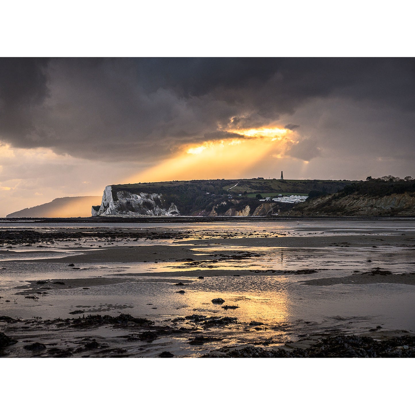 Dramatic coastline with sunrays breaking through clouds over Whitecliff Bay cliffs by a tidal flat at low light on the Isle of Wight, captured by Available Light Photography.