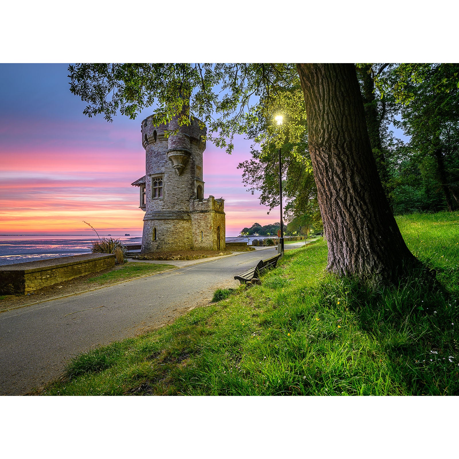 An old Appley Tower beside a path with a bench under a tree, illuminated by a street lamp at dusk with a colorful sky on the Isle. (Available Light Photography)