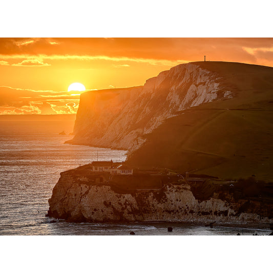 Sunset over Tennyson Down, a cliff-lined coast with a glowing sky and buildings near the water's edge on the Isle of Wight, captured by Available Light Photography.
