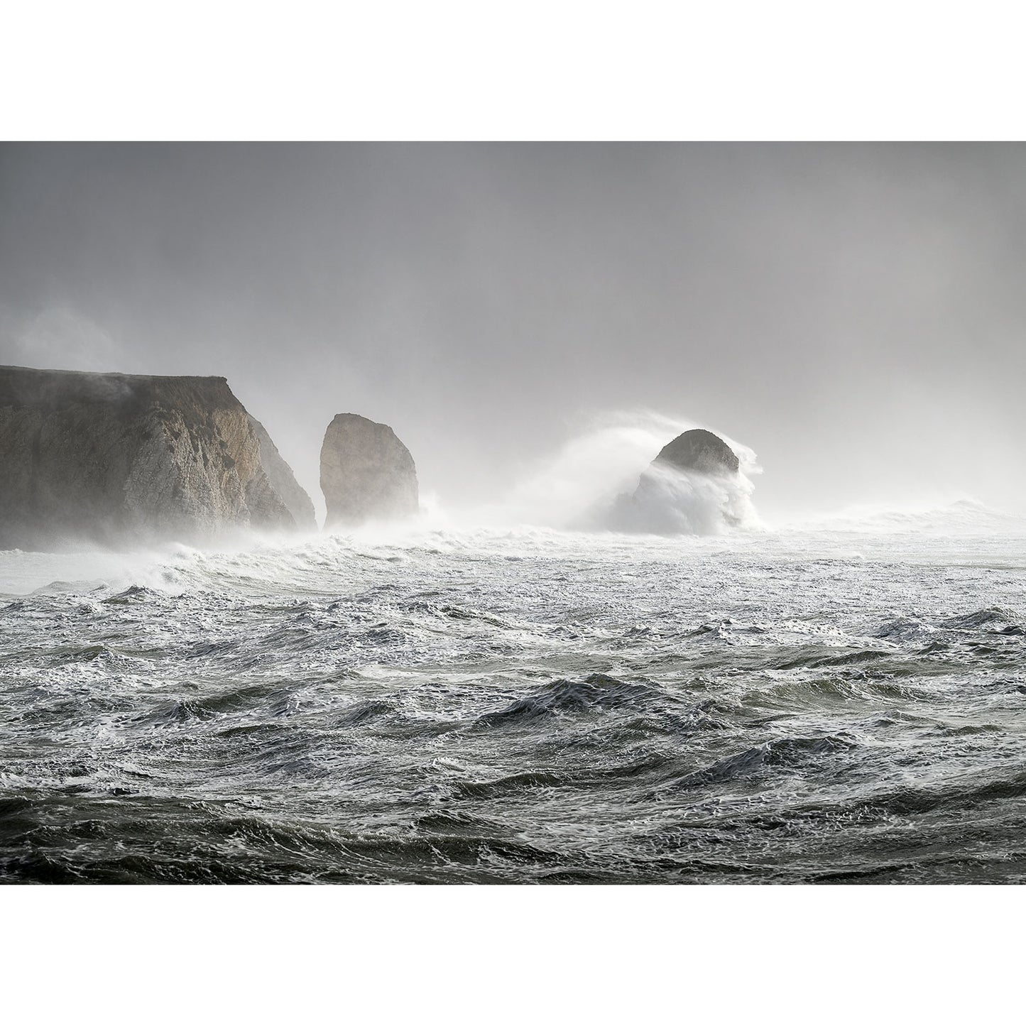 Storm Eunice with large waves breaking against cliffs under overcast skies, captured by Steve Gascoigne off the coast of Wight. - Available Light Photography