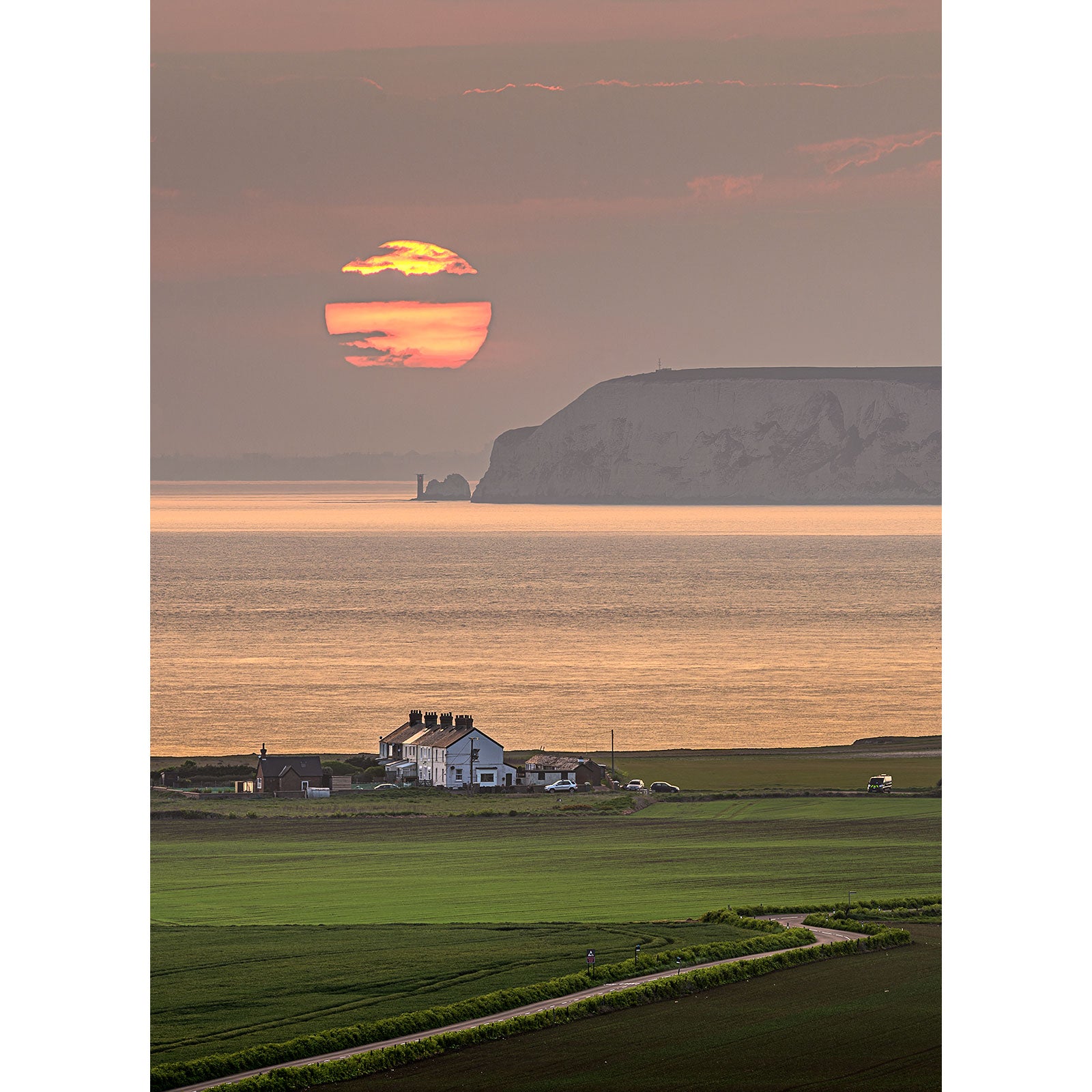 A coastal Sunset over West Wight with a house in the foreground and cliffs in the distance near Wight. Brand Name: Available Light Photography