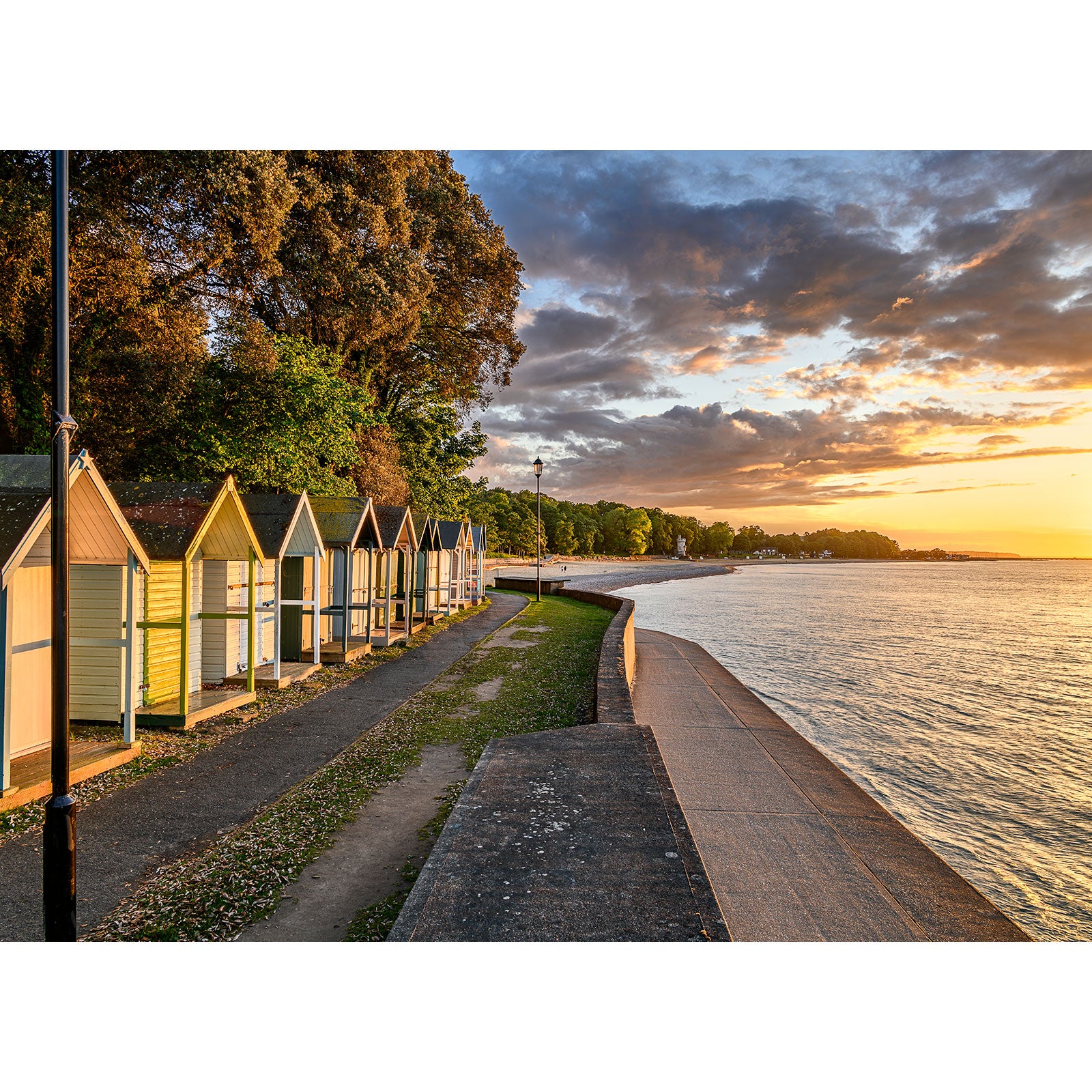 A row of colorful beach huts beside a walkway under a sunset sky at Puckpool Point on the Isle of Wight, captured by Available Light Photography.