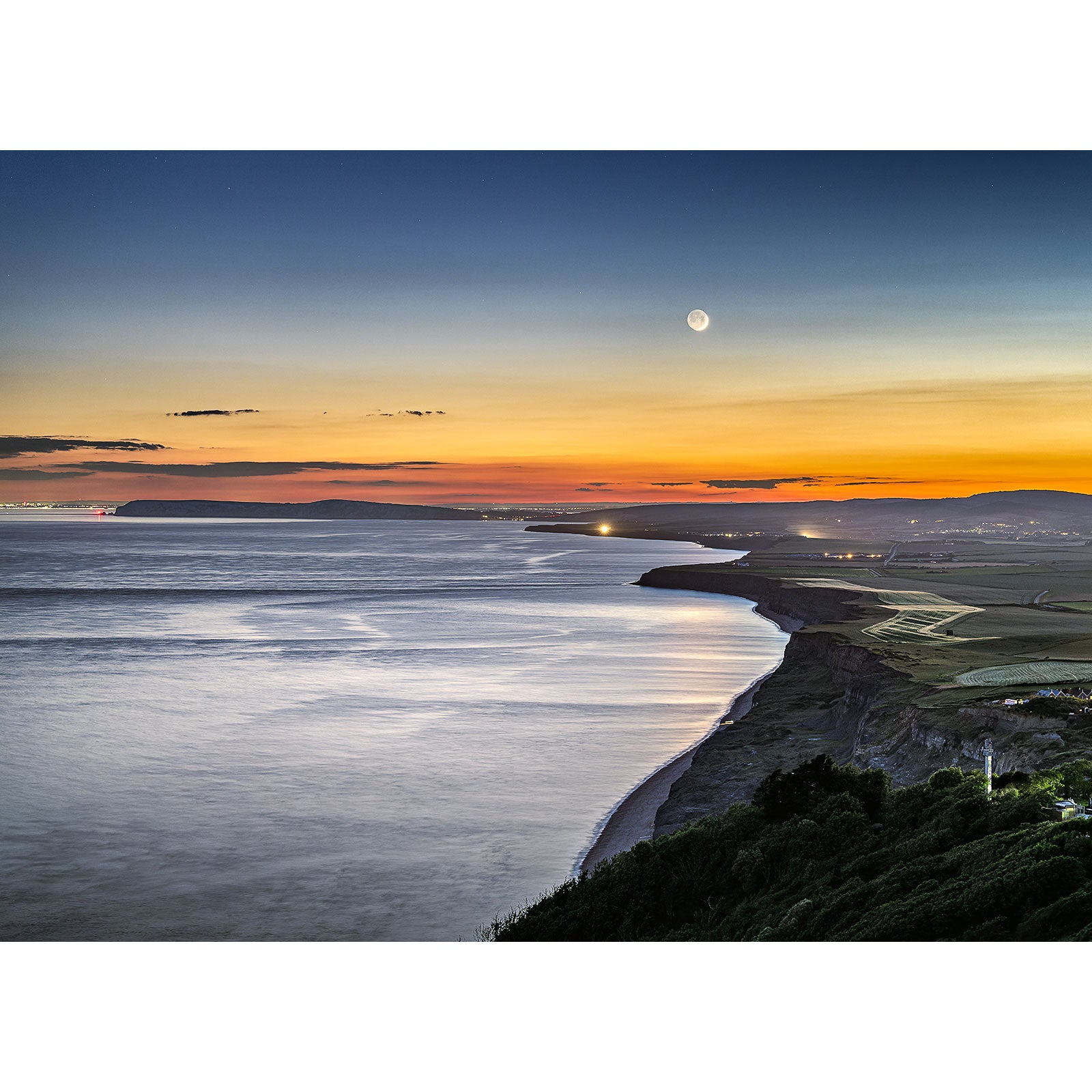A coastal twilight scene with the Crescent Moon over West Wight visible in the sky over a meandering river estuary on the Isle of Wight by Available Light Photography.