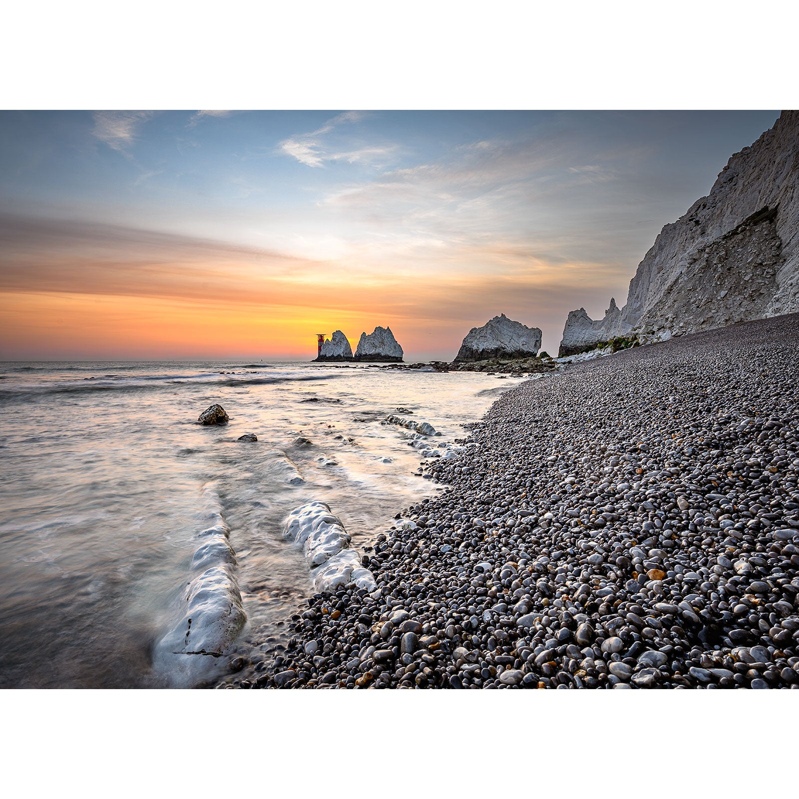 Pebble beach at sunset with cliffs and rock formations in the background, reminiscent of The Needles natural beauty by Available Light Photography.