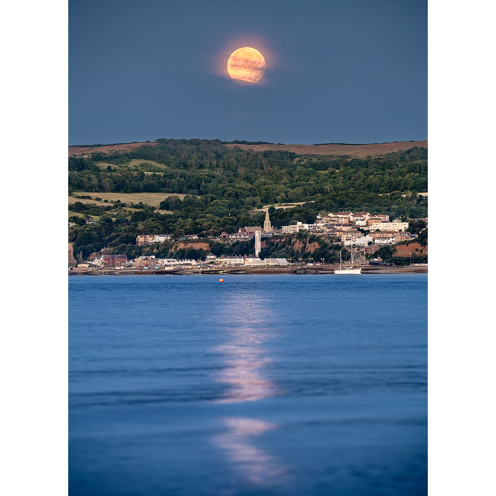 A large Moonset over Shanklin rising above a coastal town on the Isle of Wight, with its reflection on the water's surface captured by Available Light Photography.