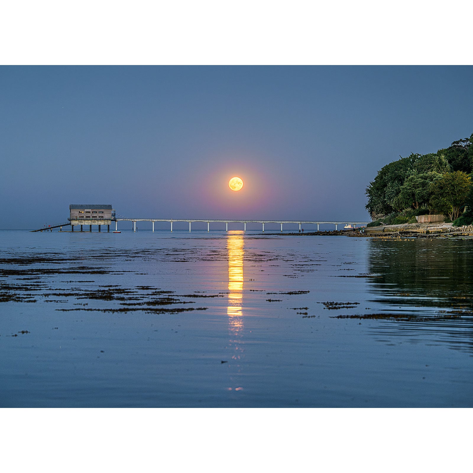 Full Moonrise over Bembridge Lifeboat Station with its reflection on the water, alongside a jetty on Gascoigne Isle by Available Light Photography.