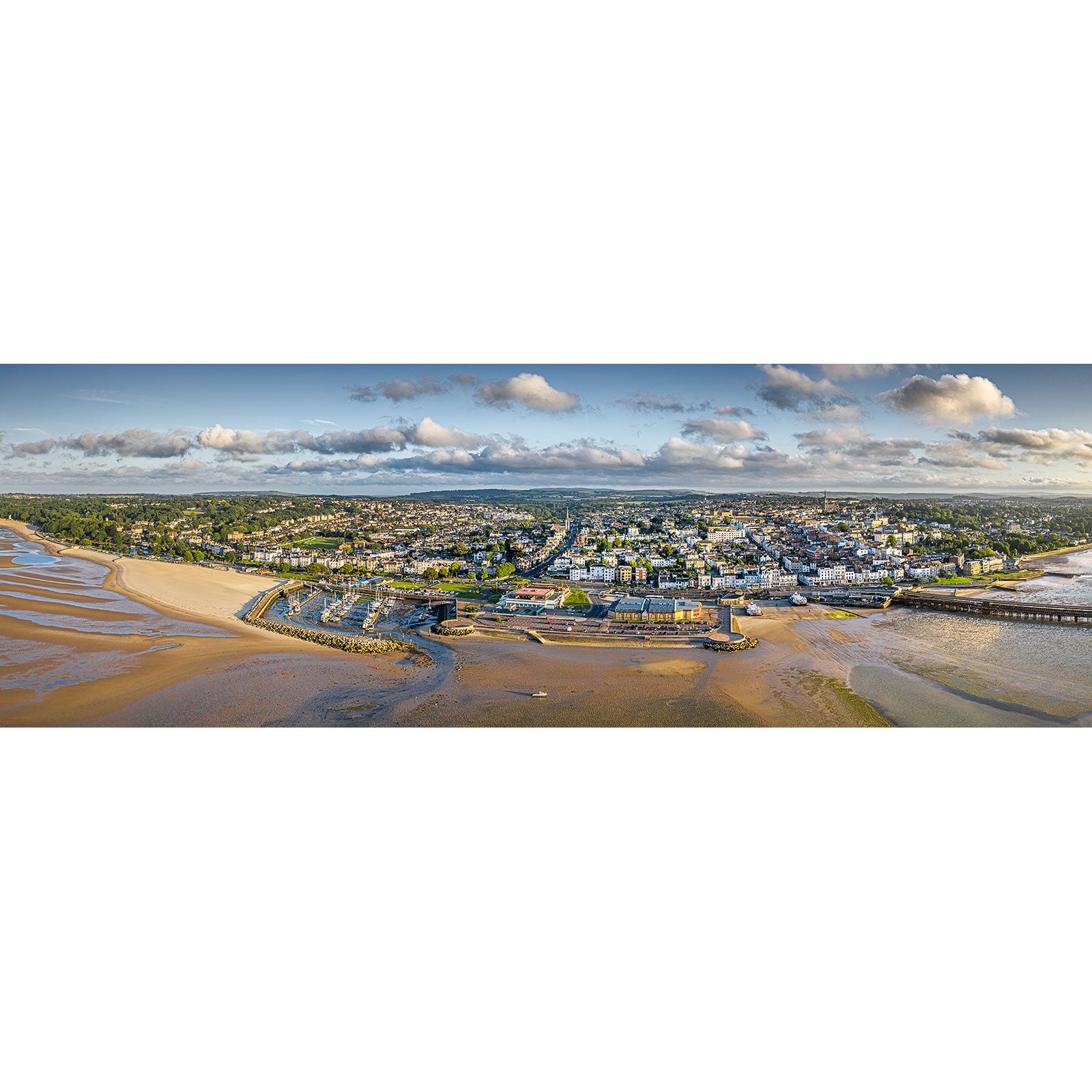 A panoramic aerial view of Ryde, a coastal town on the Isle of Wight, with sandy beaches and a pier, under a partly cloudy sky. Created by Available Light Photography.