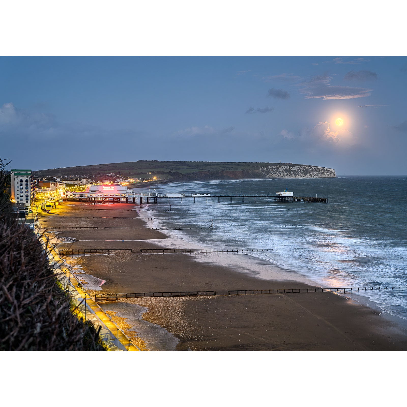 Moonrise over Sandown coastal town with illuminated Gascoigne pier and beach at twilight by Available Light Photography.
