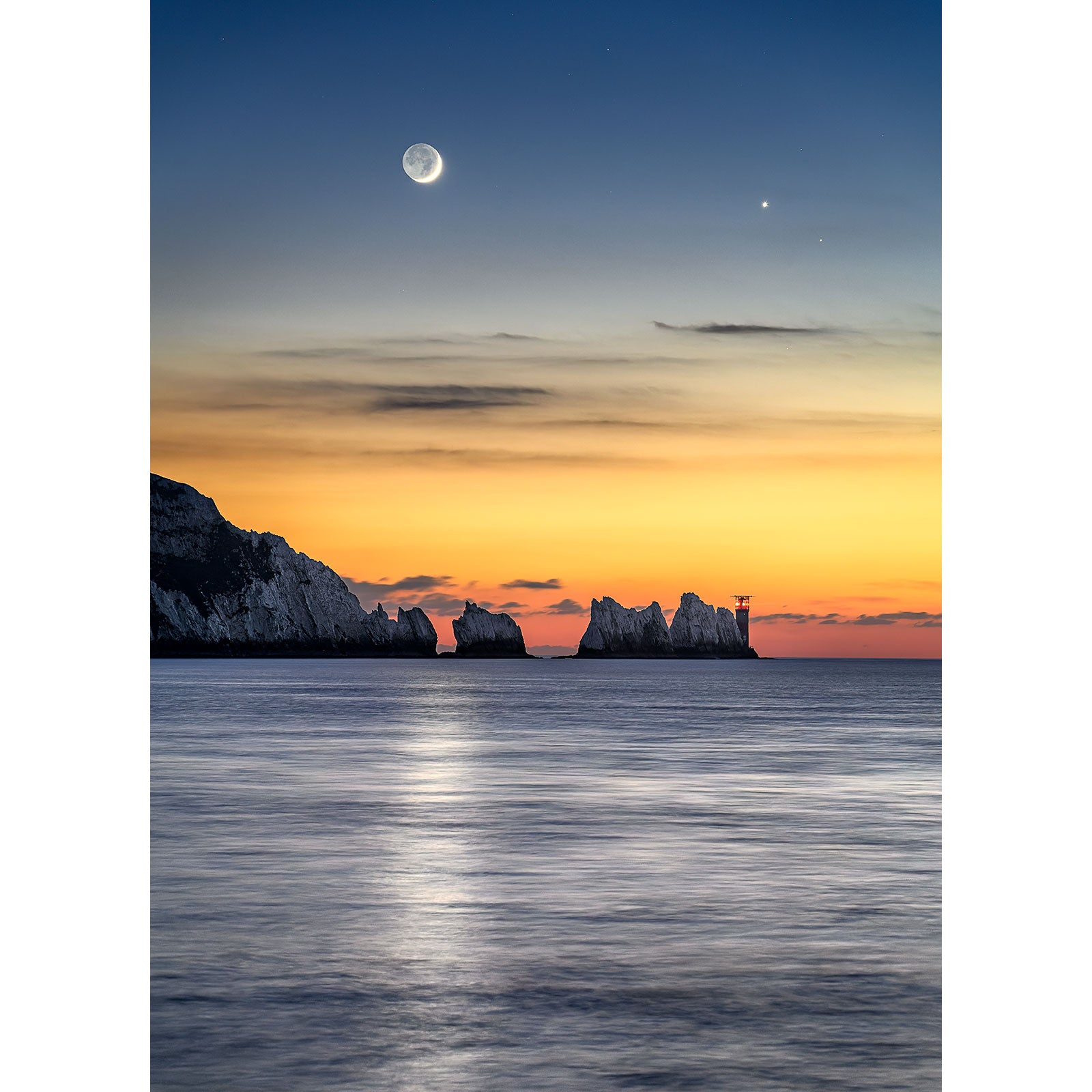 Crescent Moonset over the coastal cliffs at twilight on the Isle of Wight, with a reflection on calm sea waters by Available Light Photography.