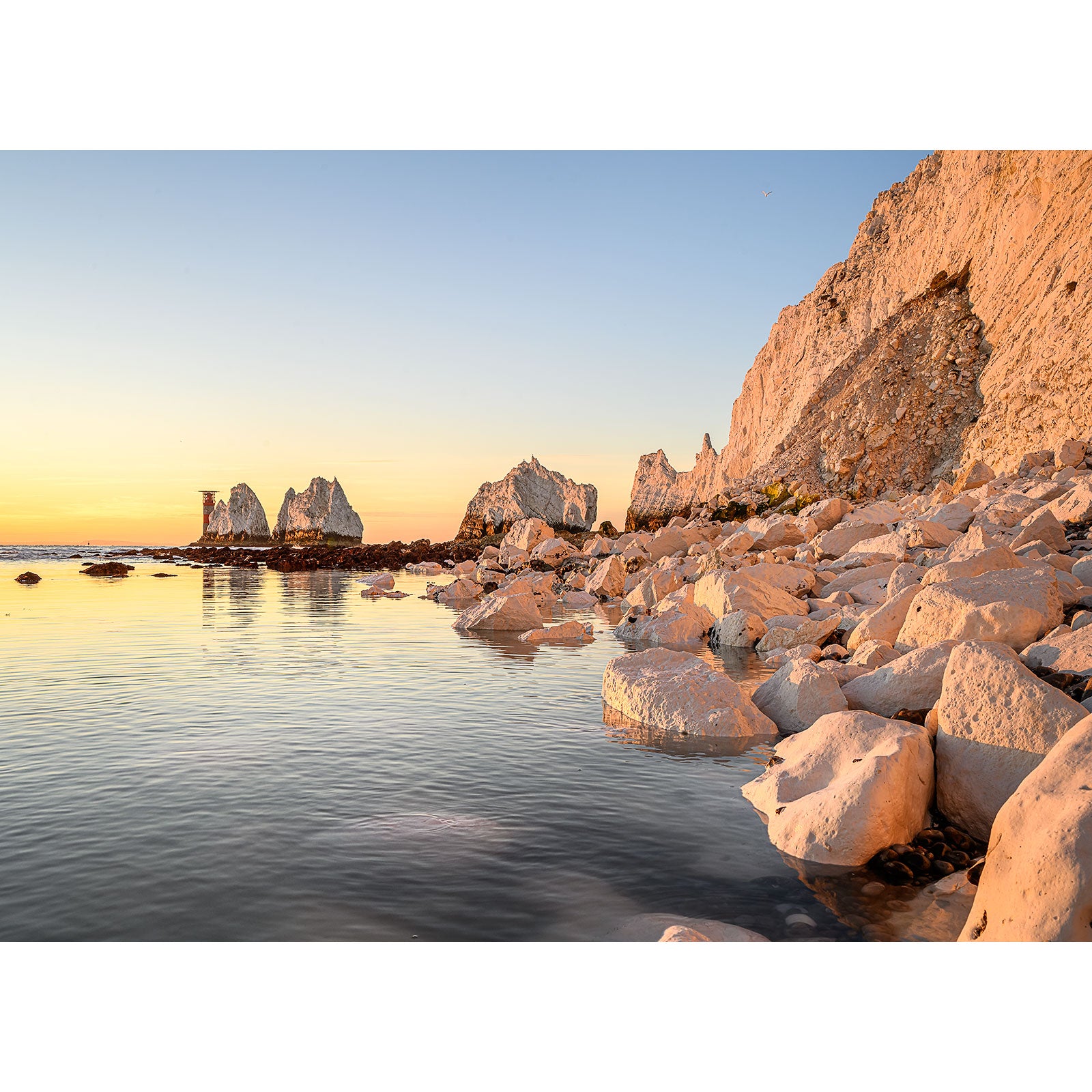 Rocky shore illuminated by golden sunset light with The Needles sea stacks in the distance on the Isle of Wight, captured by Available Light Photography.