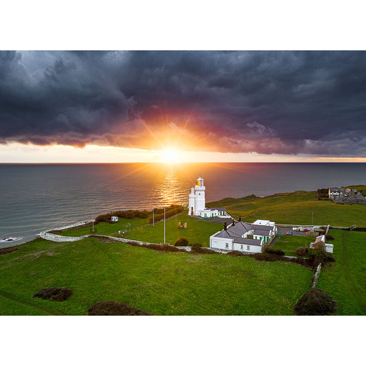 A St. Catherine's Lighthouse on a coastal headland at sunset, with the sun breaking through storm clouds over the ocean near Wight, captured by Available Light Photography.