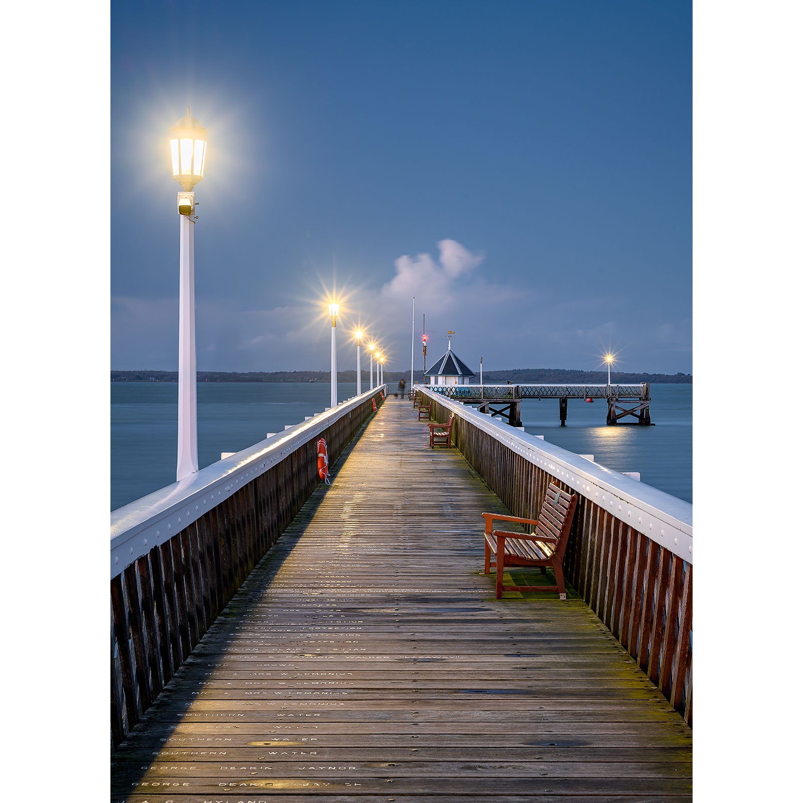 Lamps illuminate Yarmouth Pier with benches leading towards a small dock on Gascoigne Isle at dusk. (Available Light Photography)