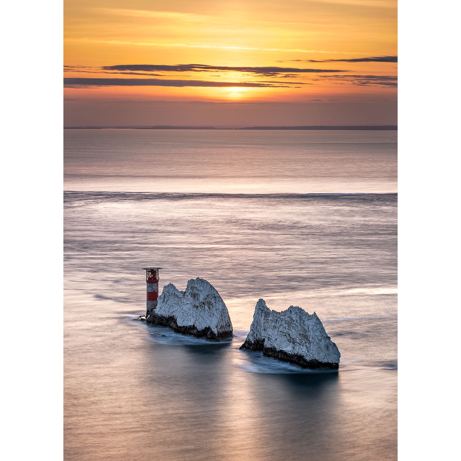 Sunset over the ocean with two rocky islets and a navigation beacon on The Needles by Available Light Photography.