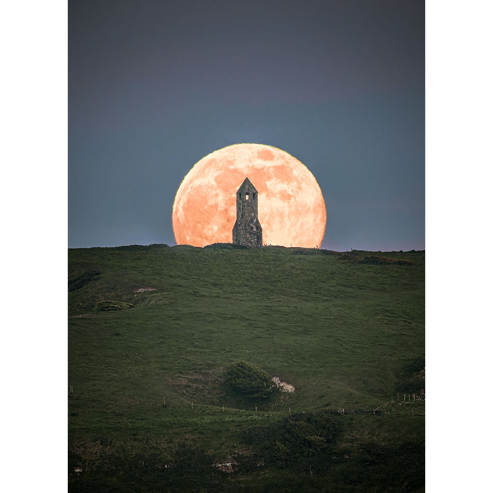 A Moonrise at St. Catherine's Oratory rises directly behind a lone tower atop a grassy hill on the Isle of Wight by Available Light Photography.