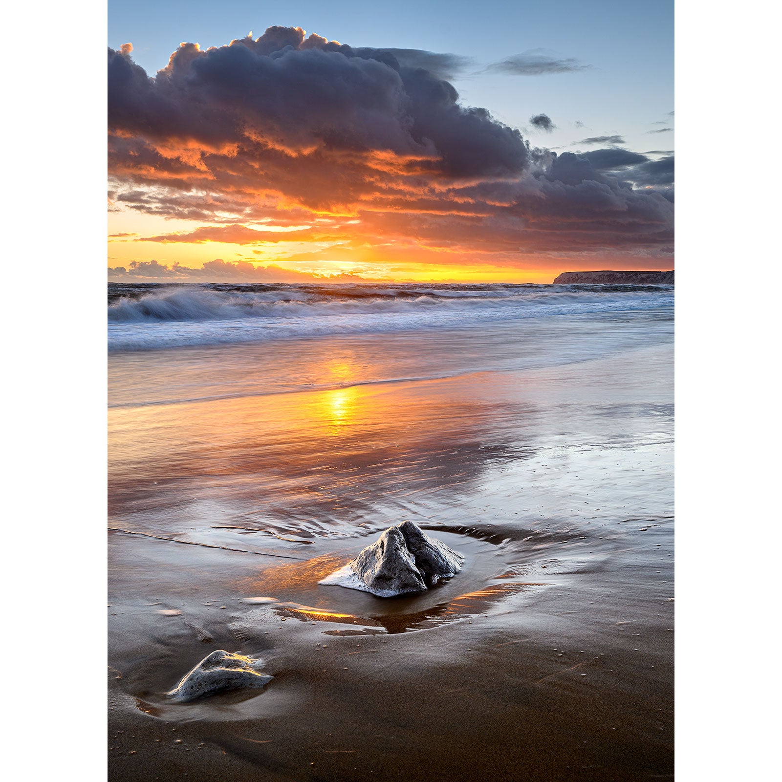 Sunset at a beach with waves and reflective wet sand, featuring rocks in the foreground named Brook Bay by Available Light Photography.